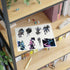 A sheet of stickers featuring various fantasy character designs, displayed on a wooden shelf next to books and office accessories.